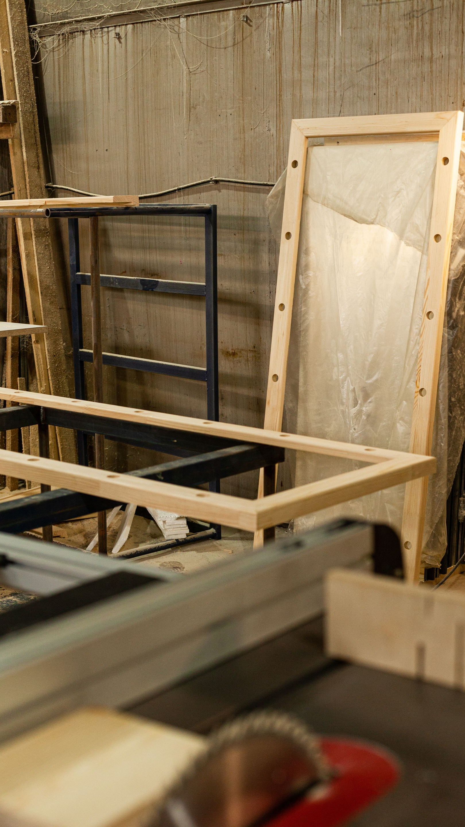 Lame de scie au premier plan, cadres en bois et étagère métallique à l'arrière-plan.