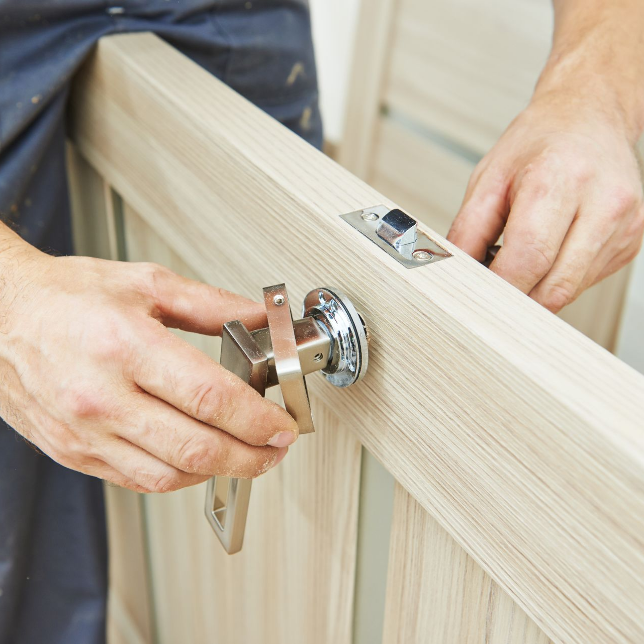 Une personne installe une poignée de porte sur un cadre de porte en bois clair.