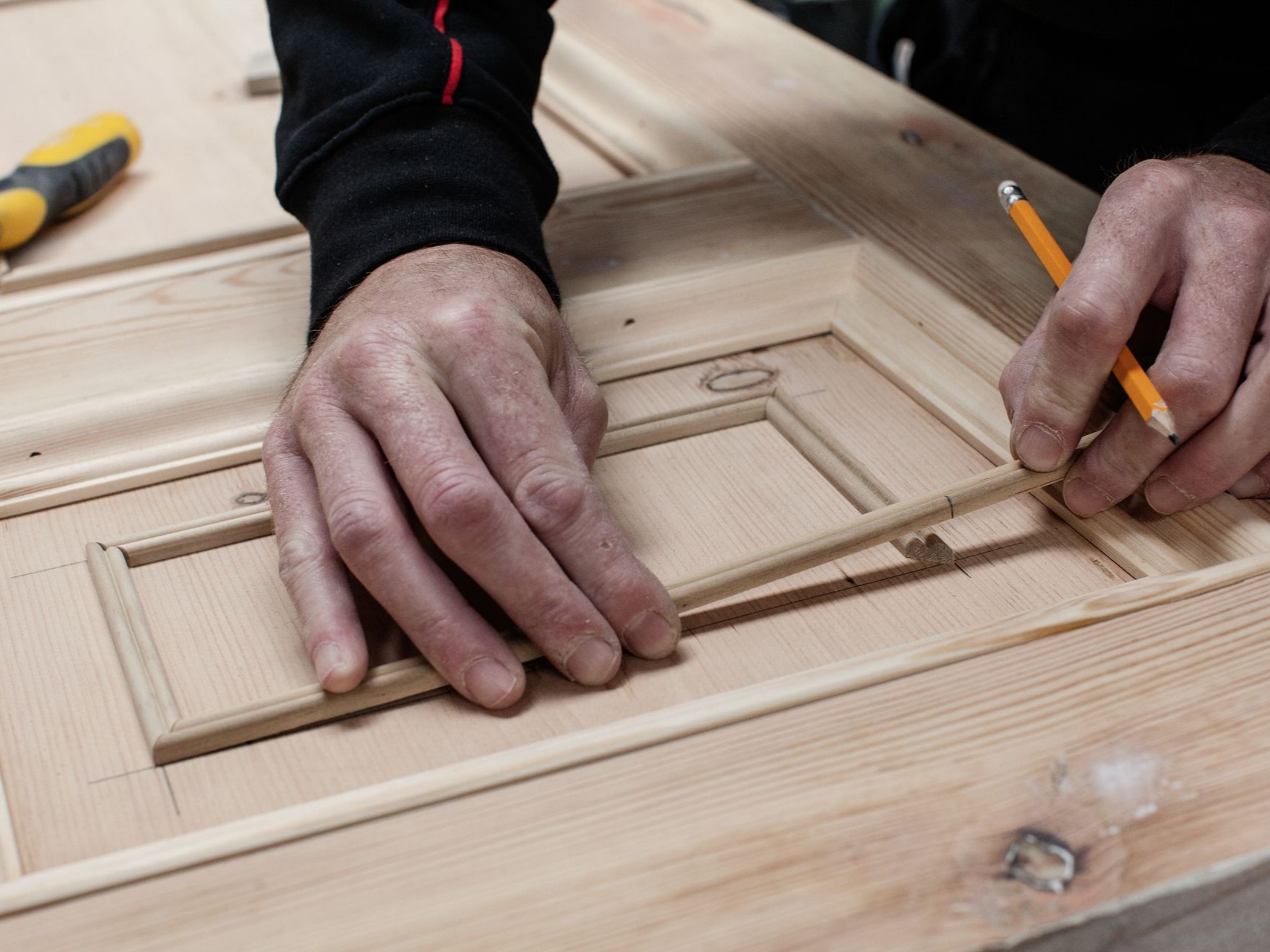 Personne utilisant un crayon pour mesurer une sculpture sur bois sur une porte en bois.