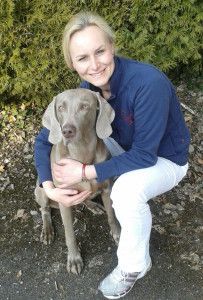 Porträt von Dr. Tanja Keller im Freien, die lächelnd einen grauen Weimaraner umarmt.
