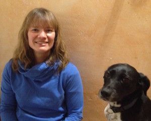 Frauke Leyendecker sitzt neben einem schwarzen Hund vor hellem Hintergrund.