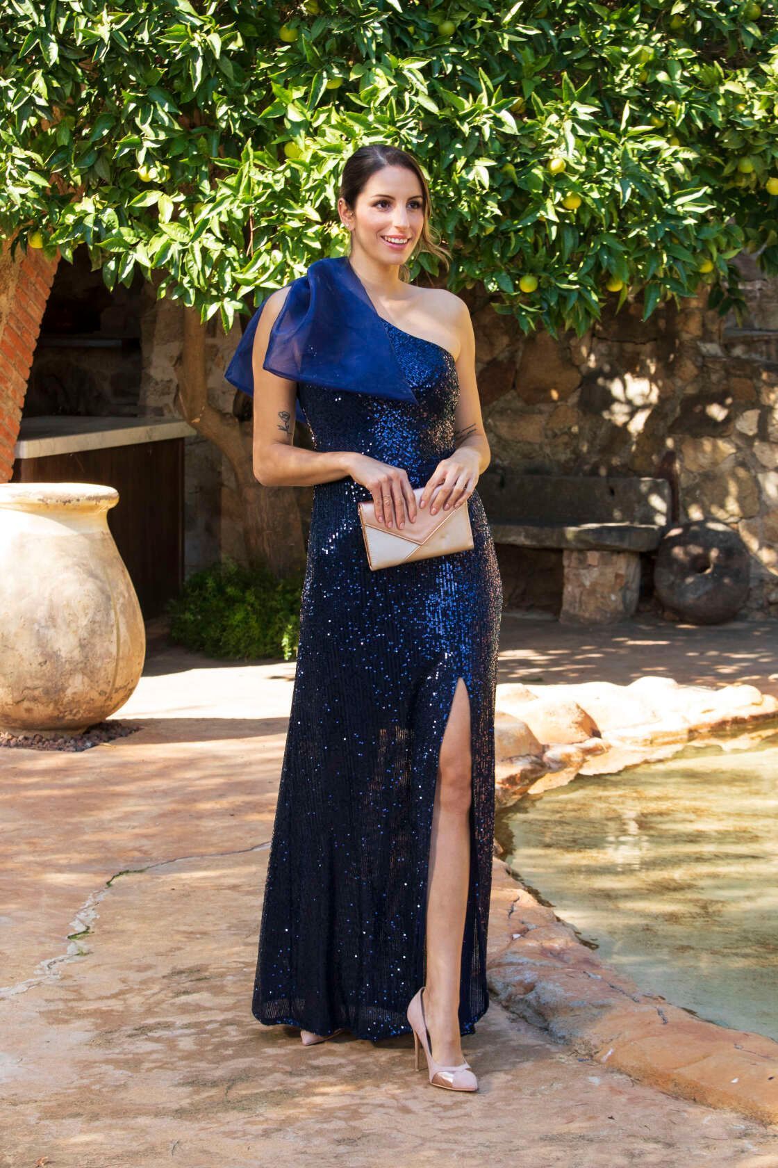 Una mujer con un vestido largo azul está parada junto a una fuente.