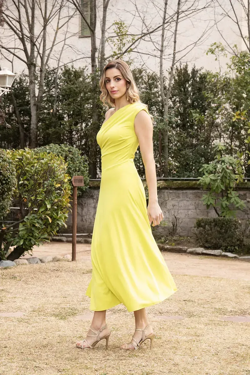 Una mujer con un vestido amarillo y tacones está parada en un campo.