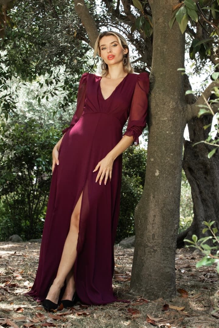 Una mujer con un vestido largo blanco está de pie junto a una valla.