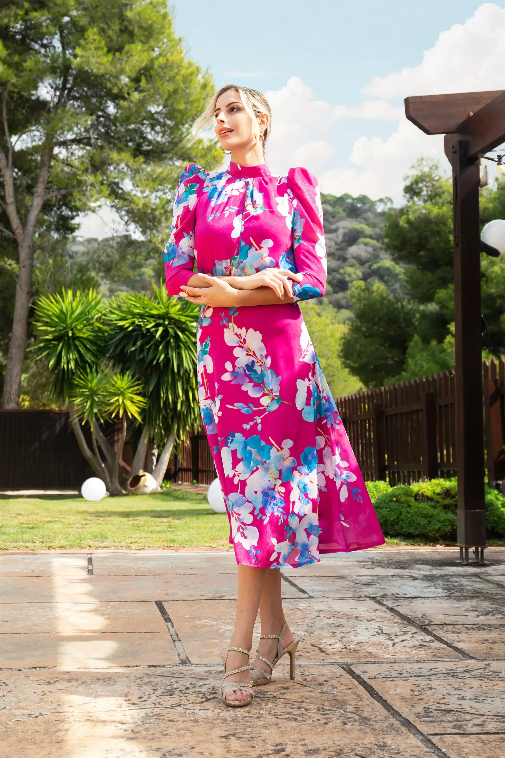 Una mujer con un vestido floral rosa está parada en una acera.
