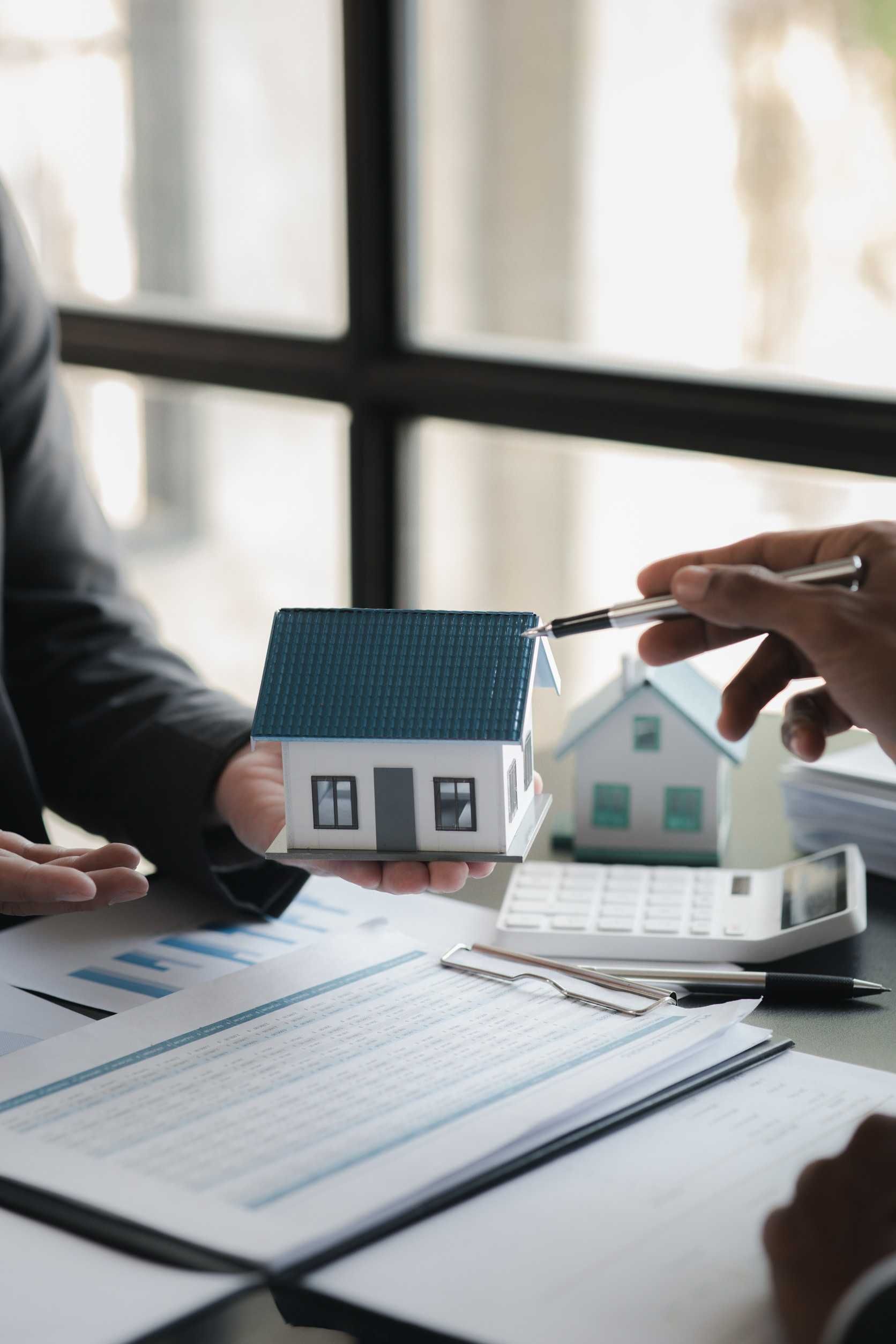 Un hombre sostiene una maqueta de casa en su mano mientras está sentado en una mesa.