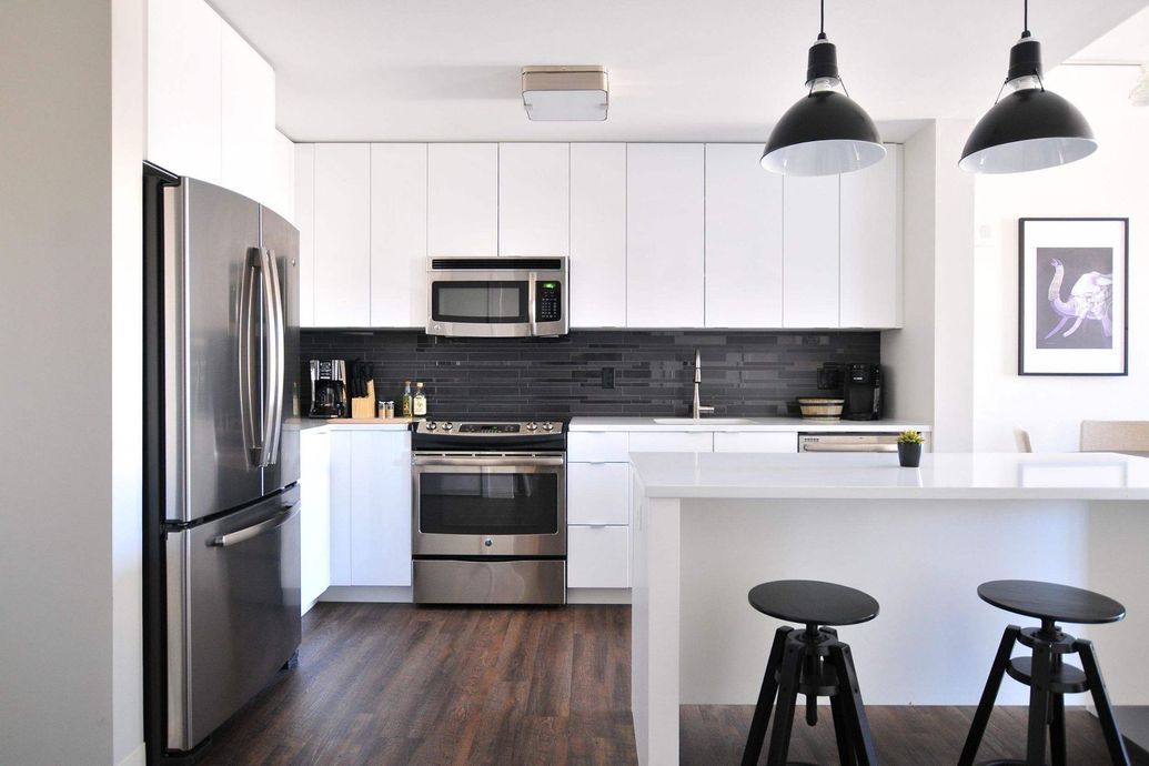 Una cocina con gabinetes blancos, electrodomésticos de acero inoxidable, refrigerador y microondas.