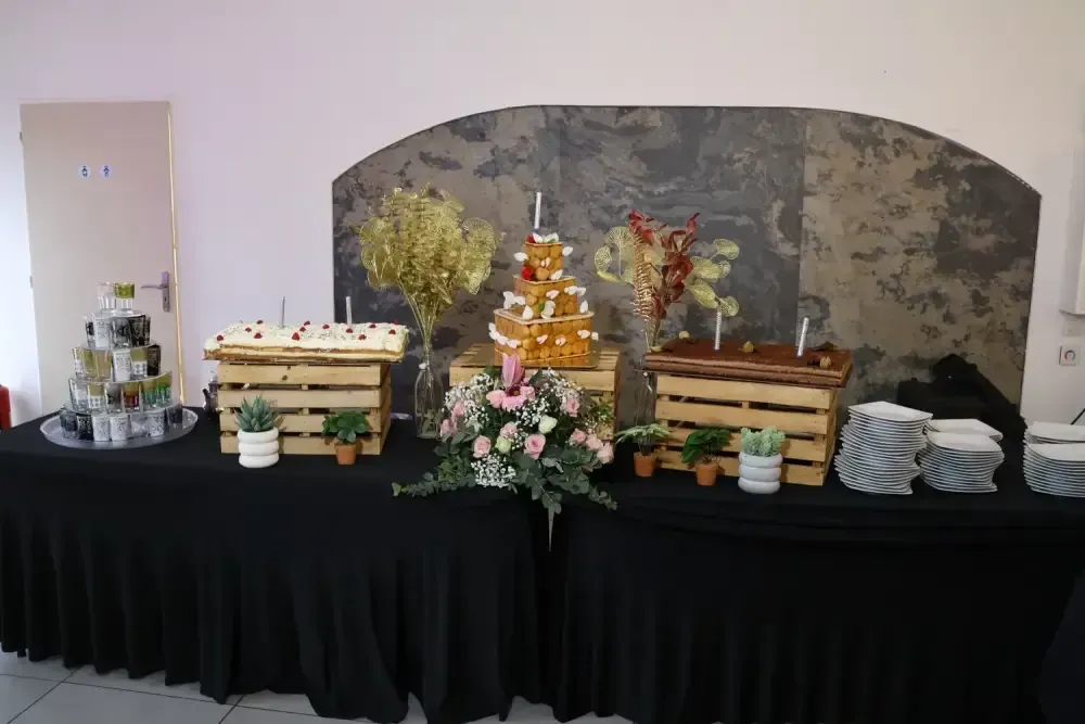 Table de buffet avec gâteaux, cupcakes, fleurs et assiettes empilées, devant un décor de fête orné
