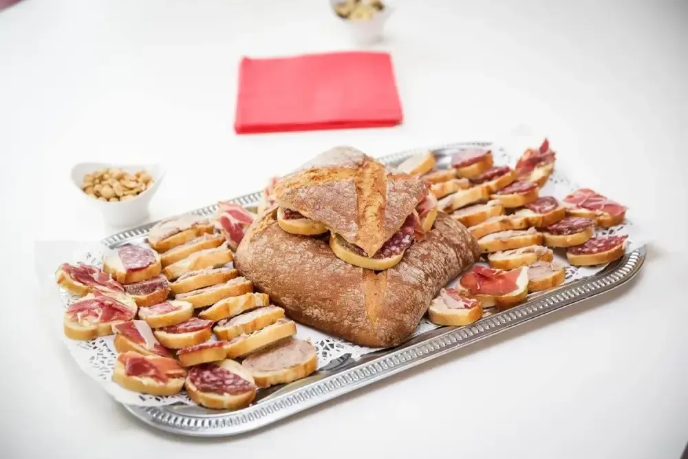 Plateau de viande rôtie et de brochettes en tranches sur une table blanche, avec une serviette rouge en arrière-plan