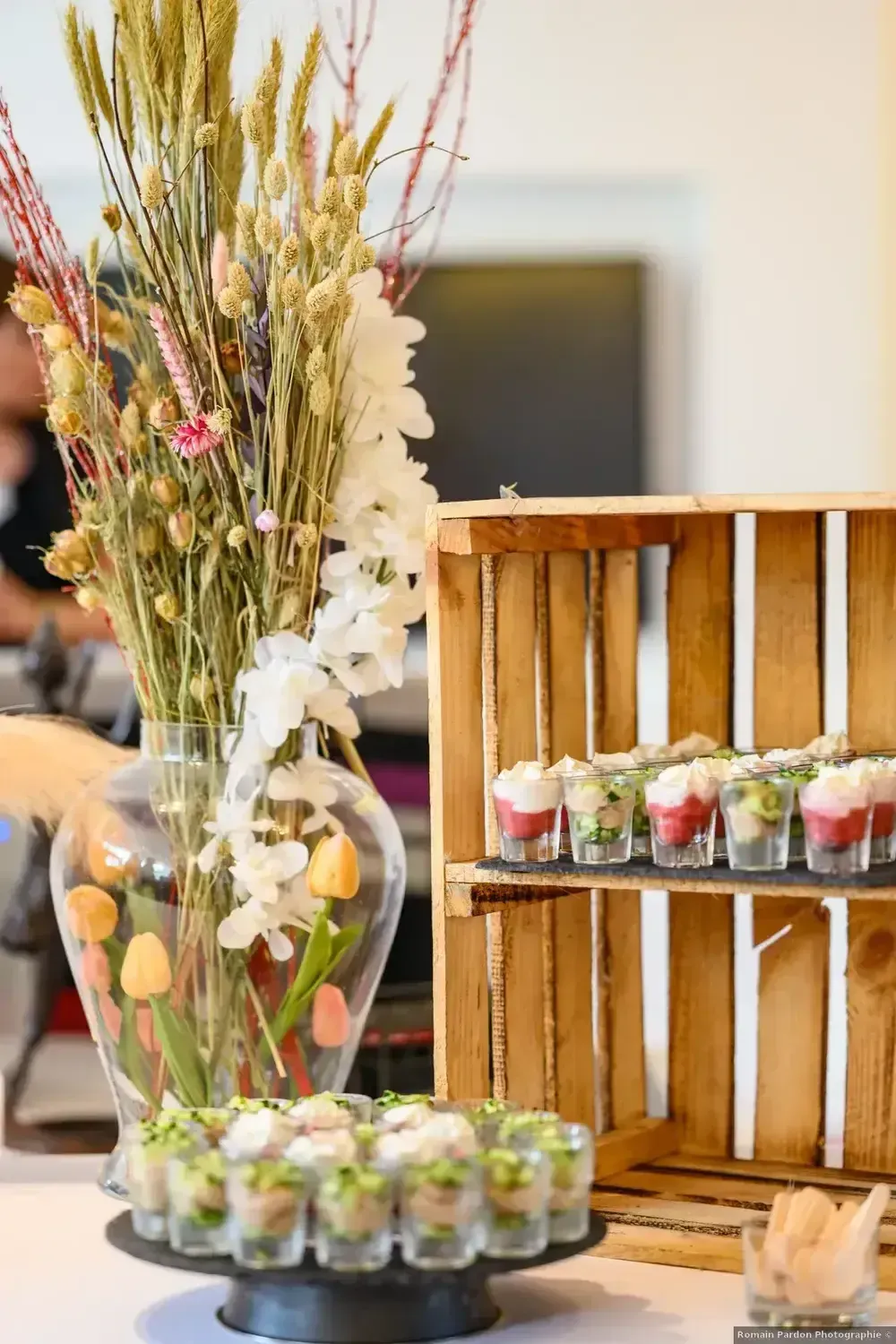Présentation de desserts avec des parfaits aux fruits, des fleurs dans un vase en verre et des plateaux en bois sur une table