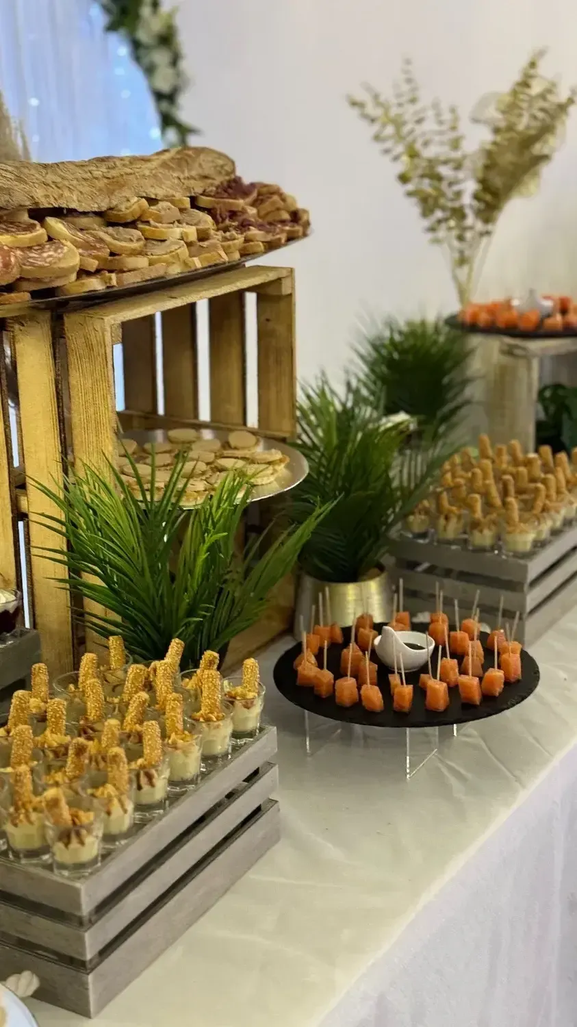 Buffet de desserts avec des plateaux de petites pâtisseries, des cupcakes et de la verdure sur une nappe blanche