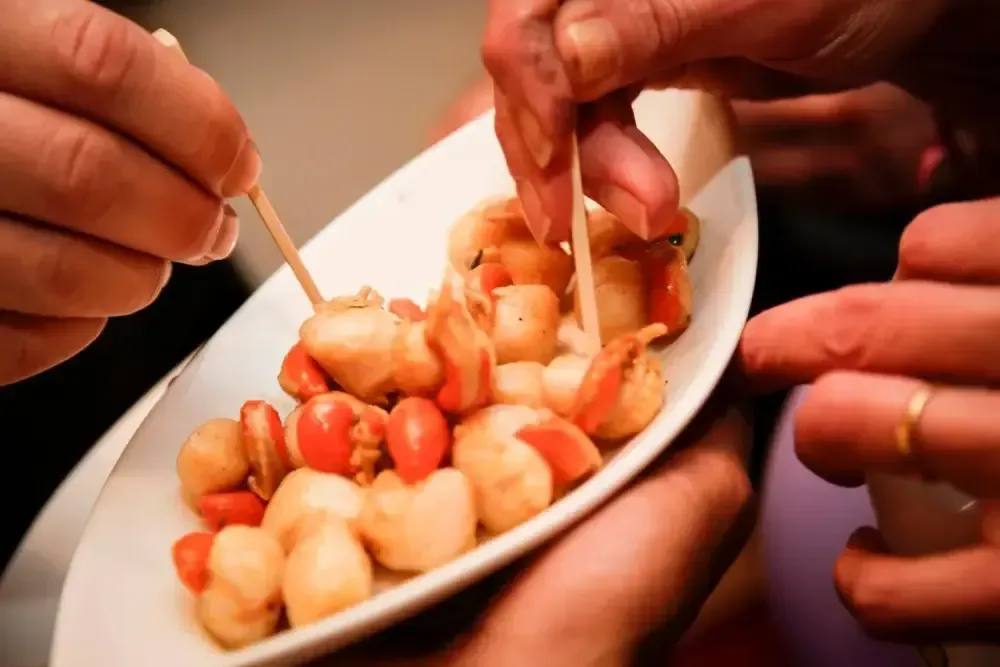 Des mains tenant des cure-dents au-dessus d’une assiette de petits amuse-bouches variés lors d’une réception mondaine