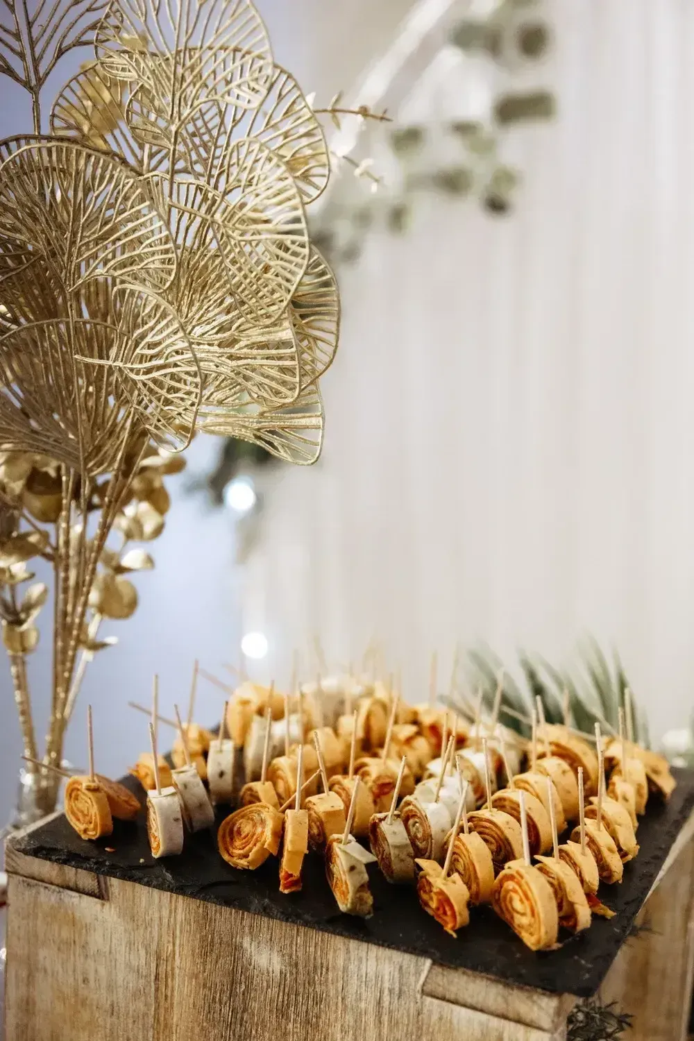 Plateau de bouchées apéritives sur des brochettes, à côté de feuilles décoratives dorées sur une table de buffet