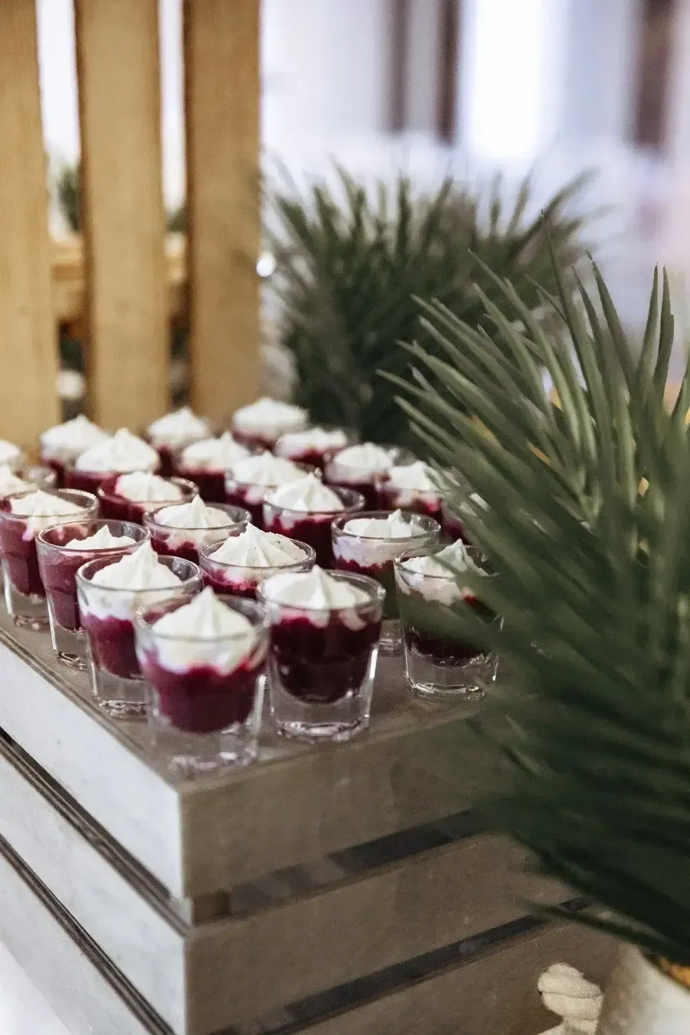 Plateau de petites verrines dessert à la crème blanche et au coulis de fruits rouges, présenté à côté de branches de pin.
