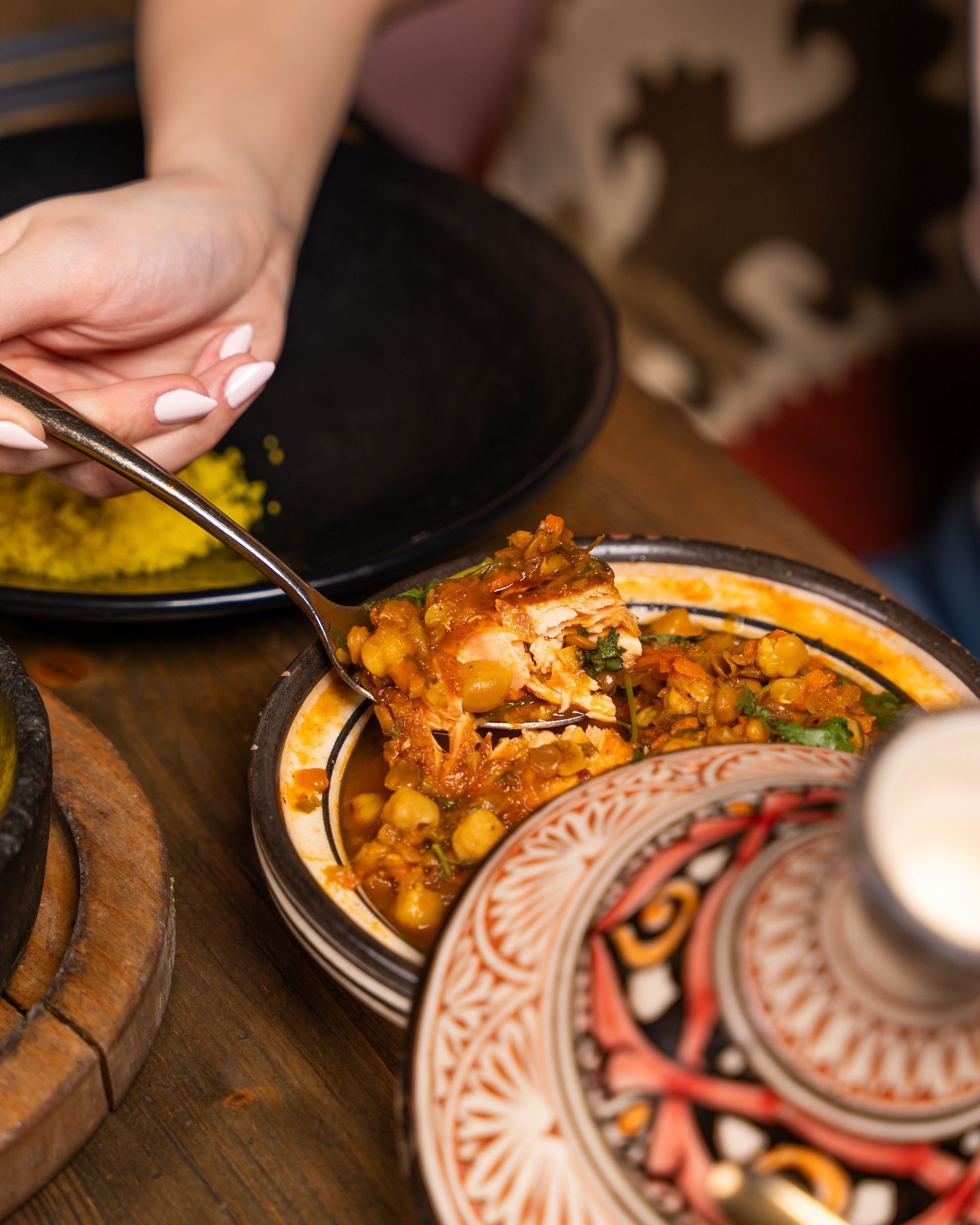 Une main s’apprête à prendre une cuillerée de curry à côté d’un plat à motifs posé sur une table à manger