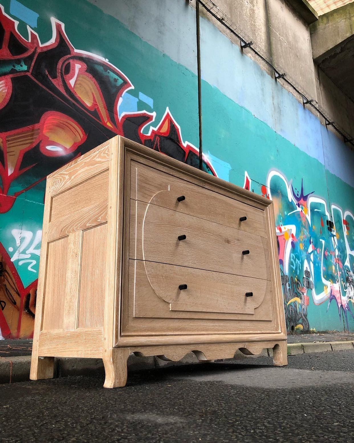 Commode en bois dans une rue, à côté d'un mur recouvert de graffitis colorés