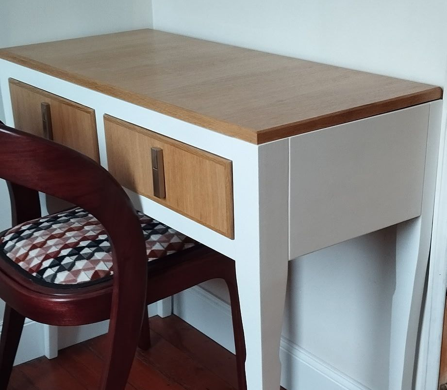 Petit bureau en bois avec tiroirs à côté d'une chaise contre un mur blanc