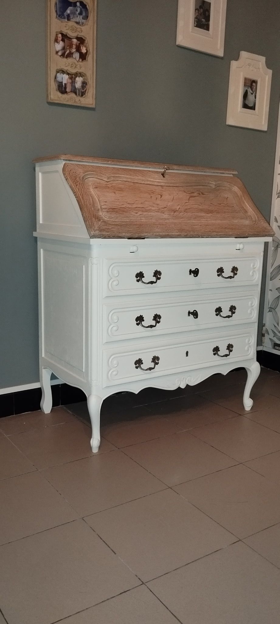 Commode vintage blanche à plateau incliné dans une pièce aux murs gris et aux photos encadrées