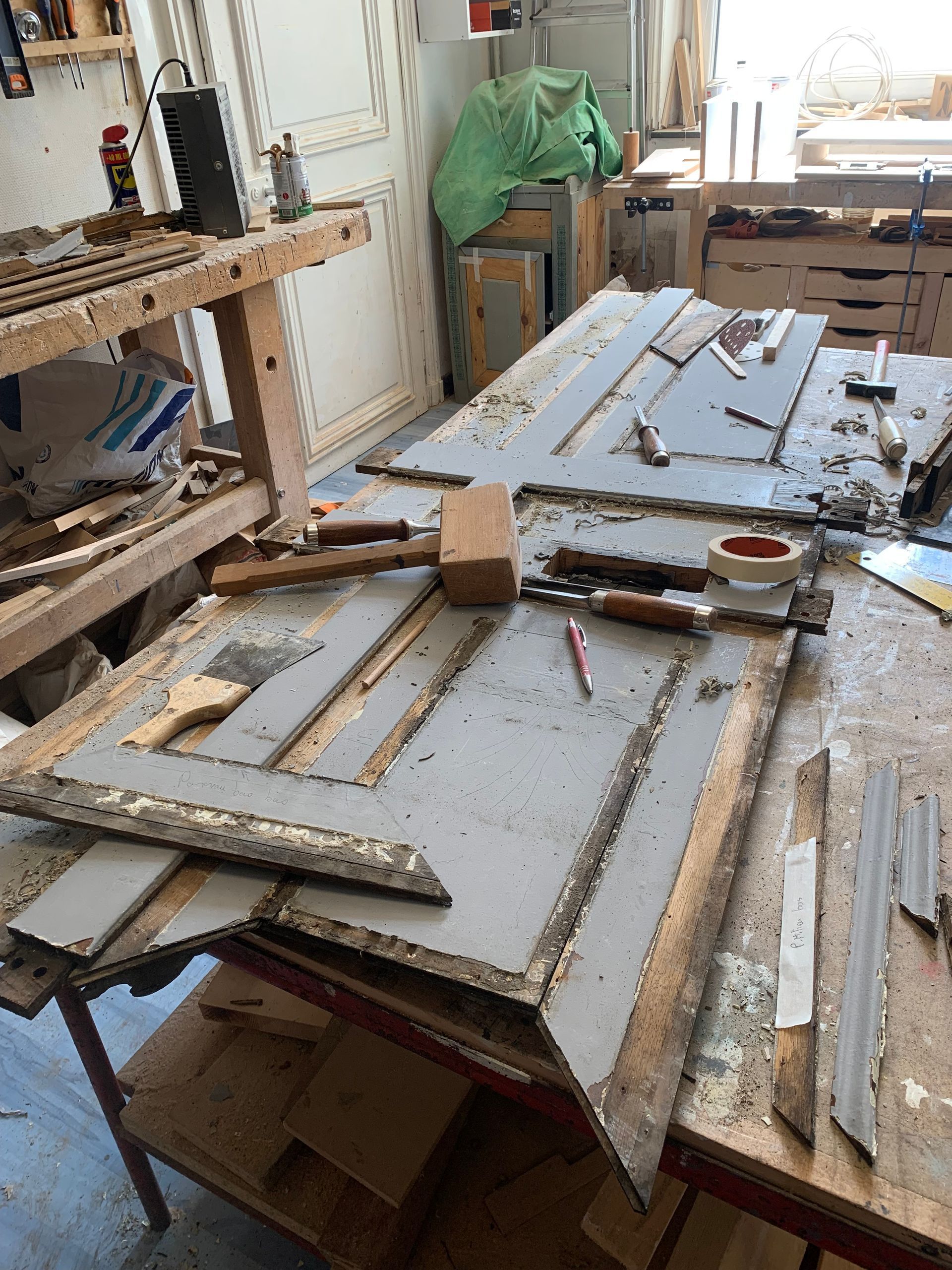 Atelier de menuiserie encombré, avec un établi recouvert de vieux cadres en bois, d'outils et de planches.