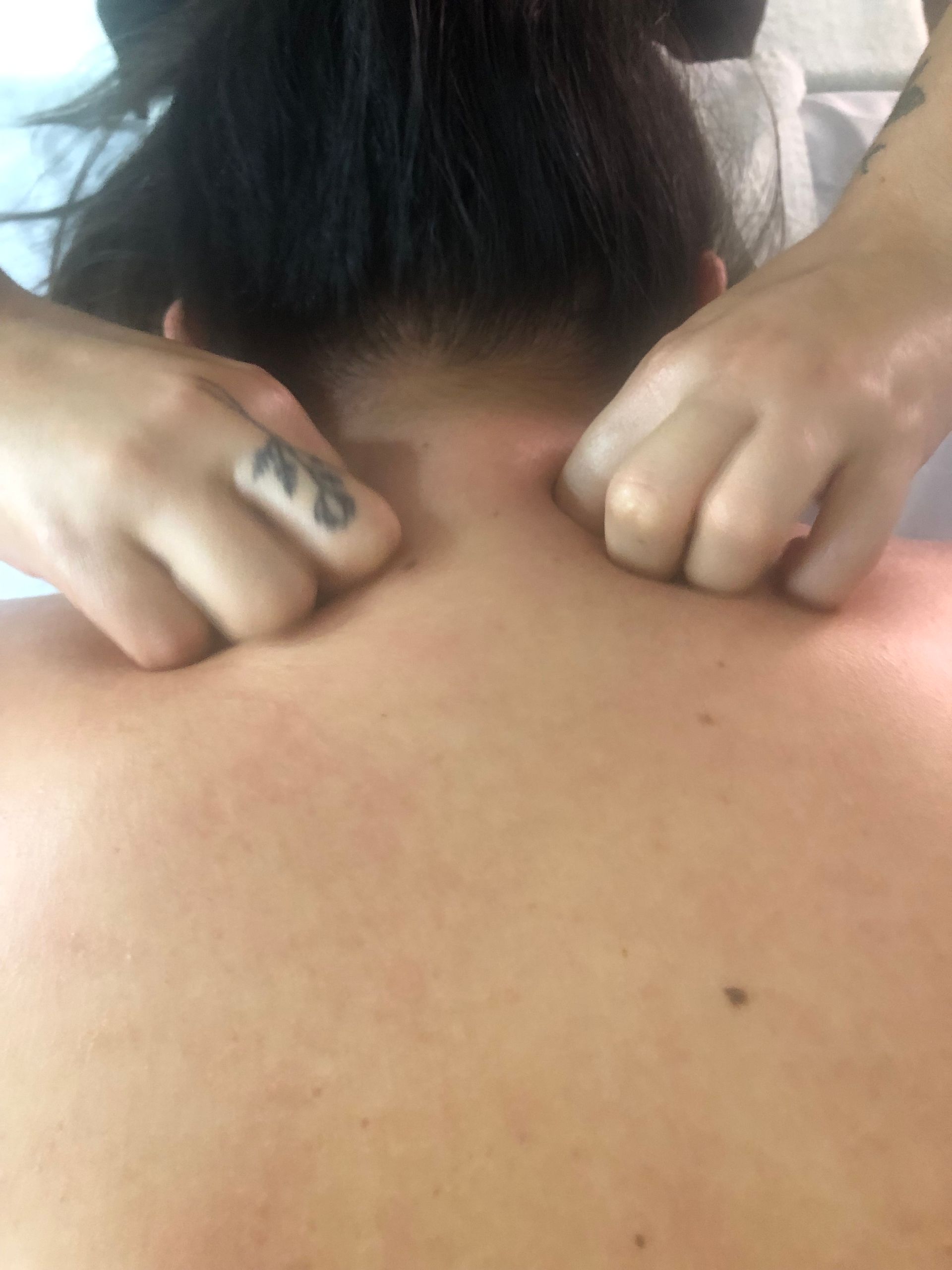 Persona recibiendo masaje de cuello de una persona con manos tatuadas, vista posterior.