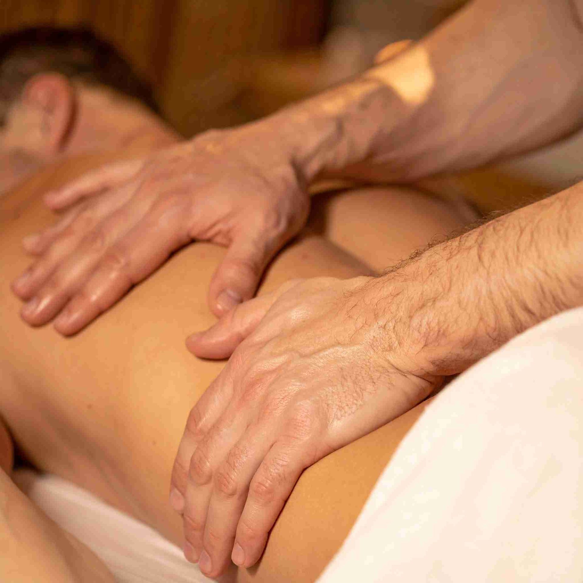 Manos masajeando la espalda desnuda de una persona, que está acostada sobre una toalla blanca.