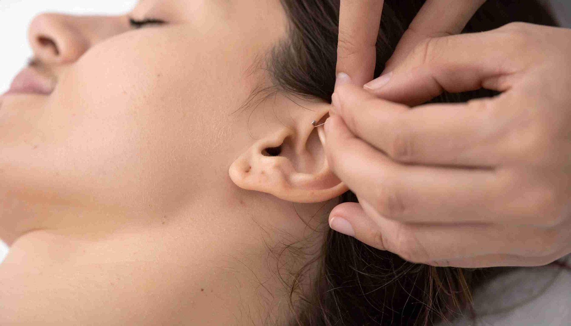 Una persona recibe acupuntura en la oreja; sus manos sostienen una aguja cerca de la oreja.