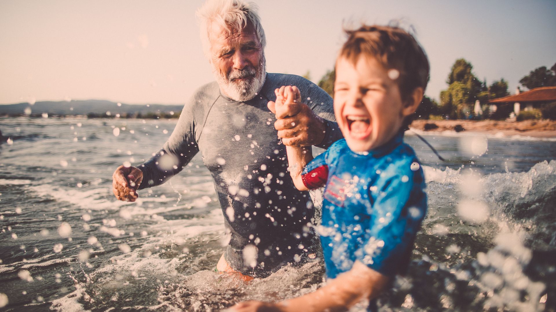 Multi-generational family laughing on a sunlit seaside terrace