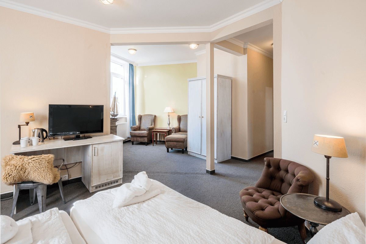 Hotelzimmer-Interieur: Bett, Schreibtisch mit Fernseher, Sitzecke mit Stühlen, neutrale Farben.