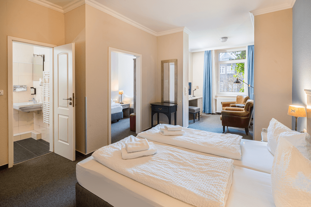 Hotelzimmer mit zwei Einzelbetten, einem Badezimmer und einer Sitzecke mit Fenster.