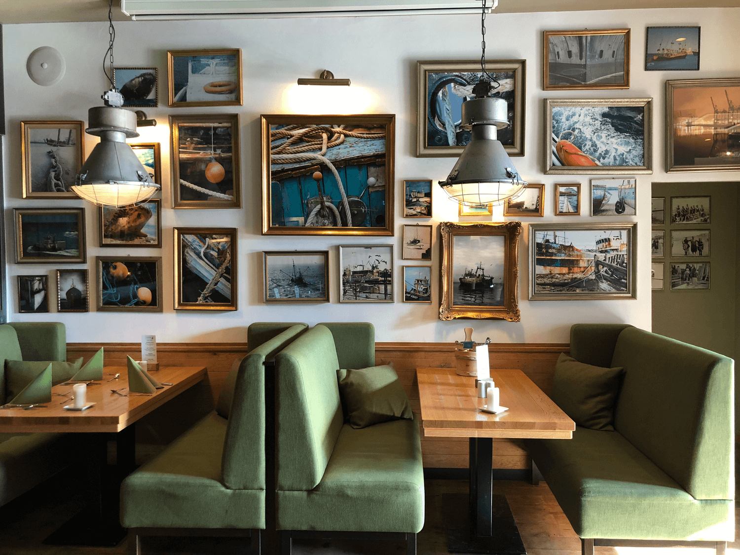 Restaurantinterieur mit Sitznischen und Holztischen, verziert mit gerahmten maritimen Bildern und Pendelleuchten.