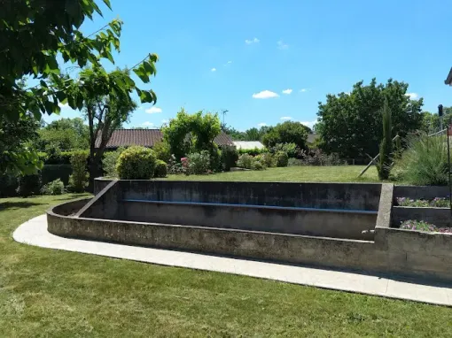 Un bassin rectangulaire en béton se dresse au milieu d'une pelouse verdoyante, par une journée ensoleillée sous un ciel bleu parsemé de nuages épars.