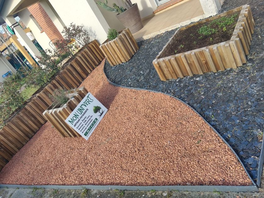 Un aménagement de jardin avec des jardinières en bois, du gravier gris foncé et une zone incurvée de gravier rouge, surmontée d'une enseigne commerciale.