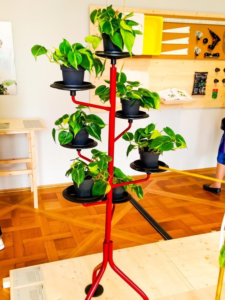 Design-Pflanzenregal mit spiralförmig angeordneten Pflanztöpfen auf rotem Gestell.