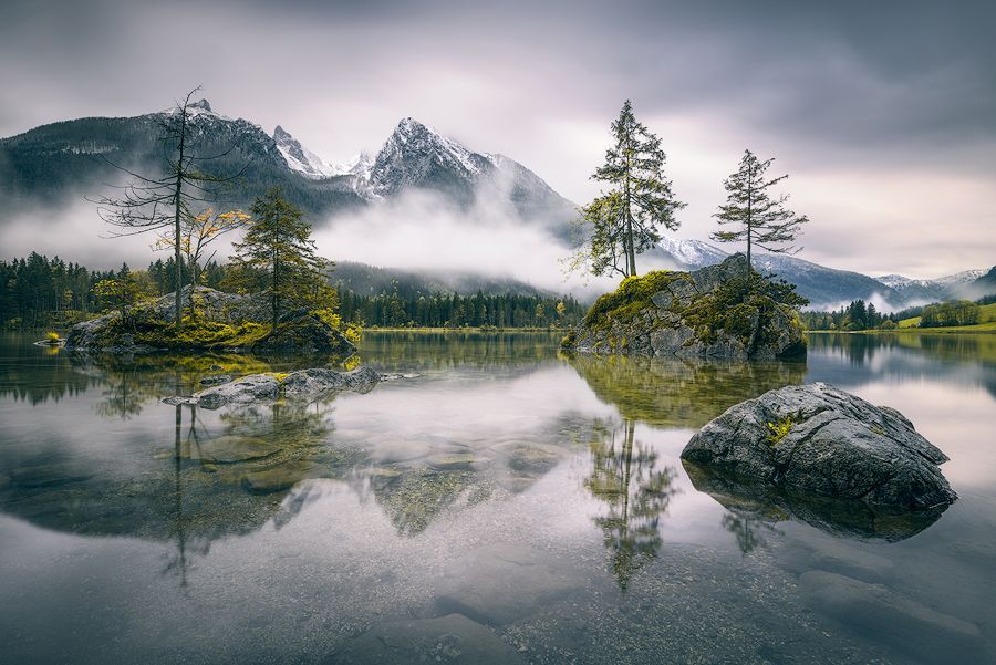 Felsinsel mit Tannen in einem spiegelglatten Bergsee, Naturidylle pur.