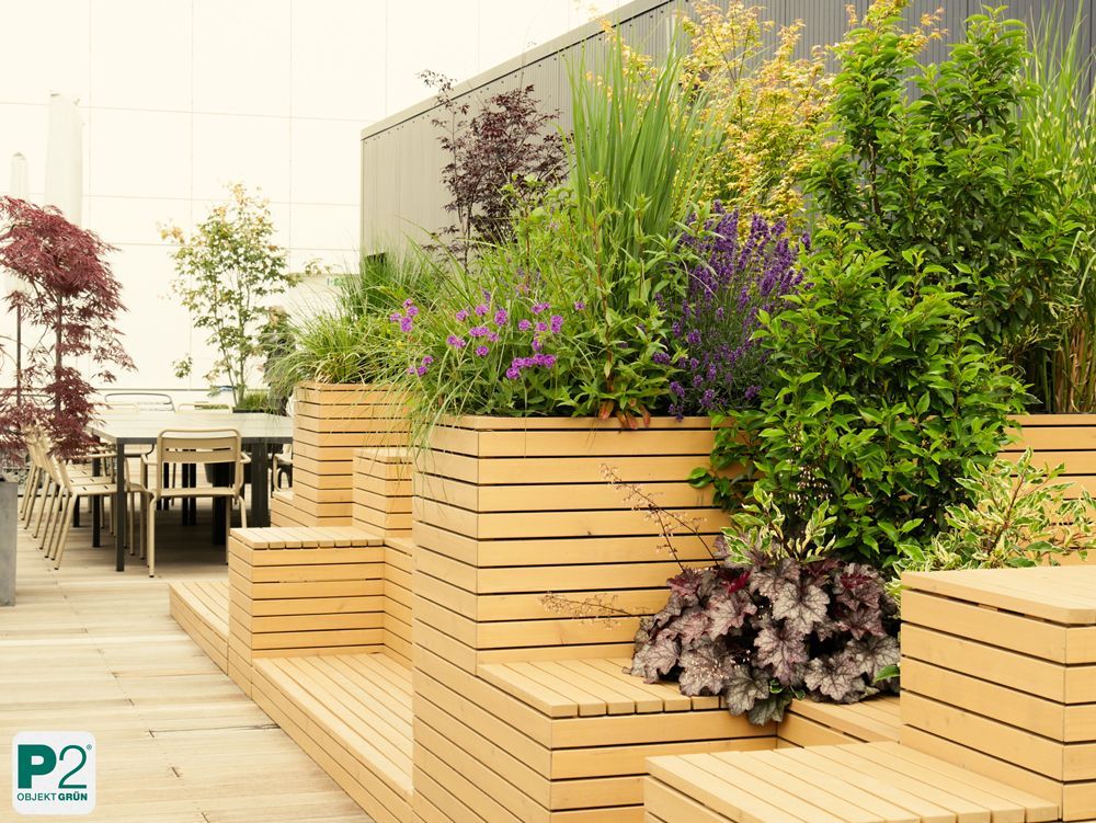 Begrünter urbaner Sitzbereich mit Hochbeeten, Pflanzen und Tischgruppe im Freien.