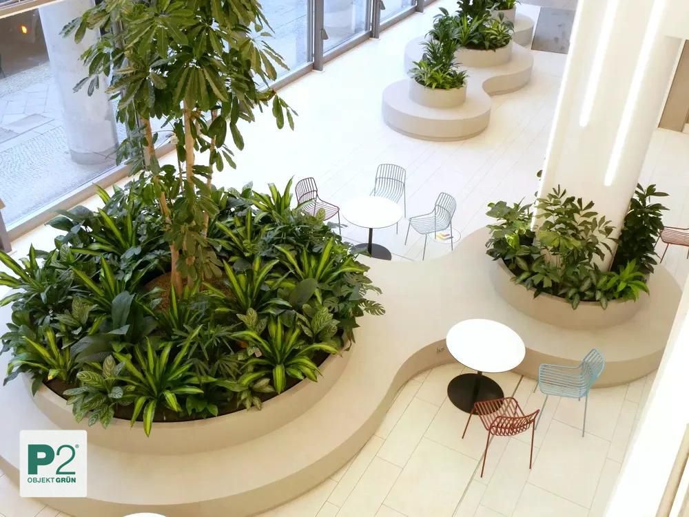 Innenraum mit geschwungenen Pflanzbeeten, grünen Pflanzen und Sitzgruppen mit Tischen und Stühlen von P2 Objekt Grün