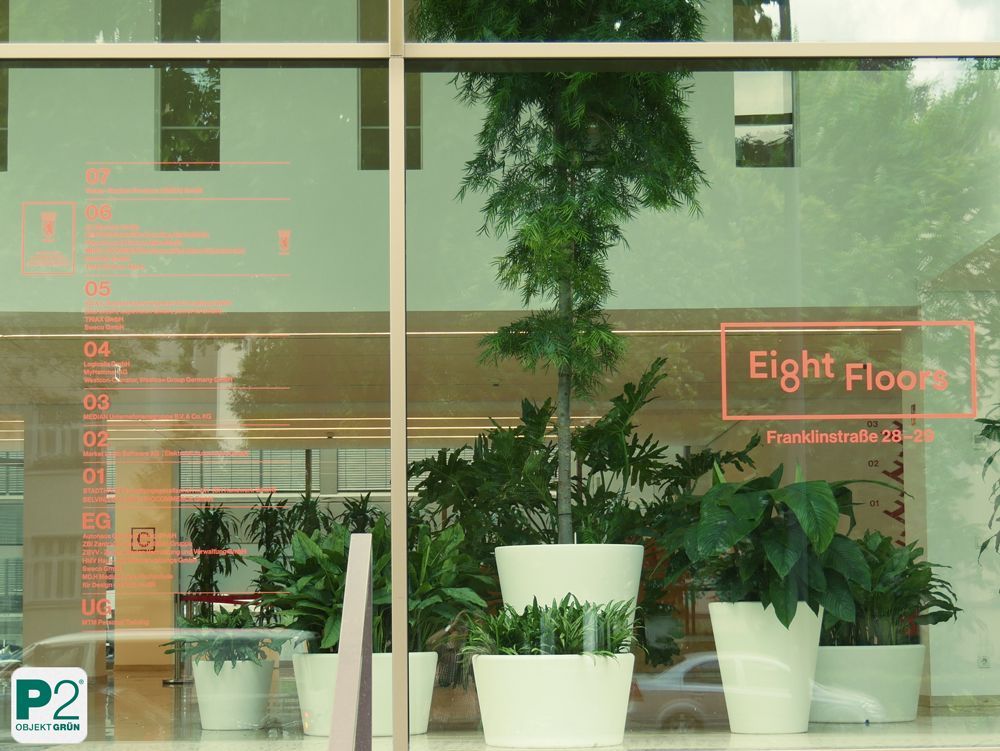 Ansicht des Acht-Etagen-Gebäudes mit Pflanzen im Vordergrund.