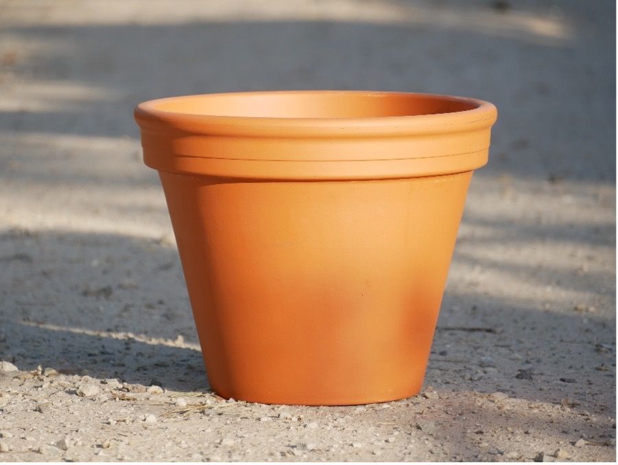 Klassischer leerer Terrakottatopf auf trockenem Erdboden im Sonnenlicht.