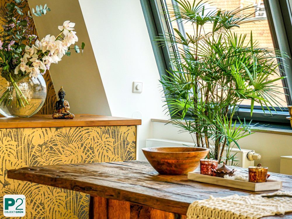 Wohnzimmer mit rustikalem Holztisch, grüner Zimmerpflanze, Blumenvase und Buddha-Figur auf Kommode