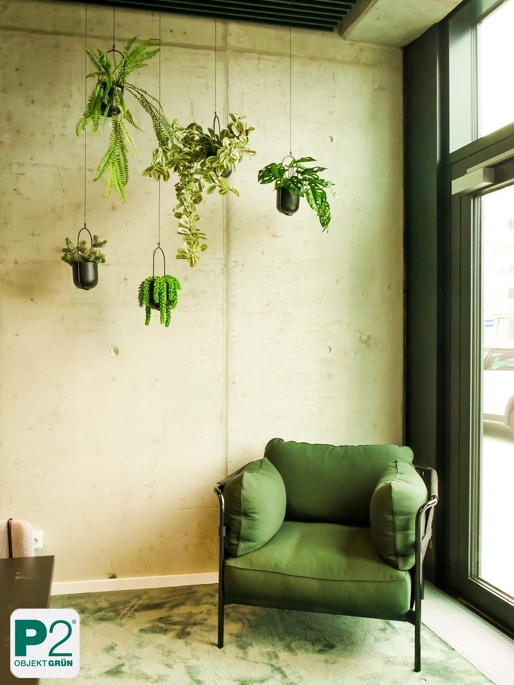 Grüner Wohnraum mit hängenden Pflanzen und einem gemütlichen Sessel.