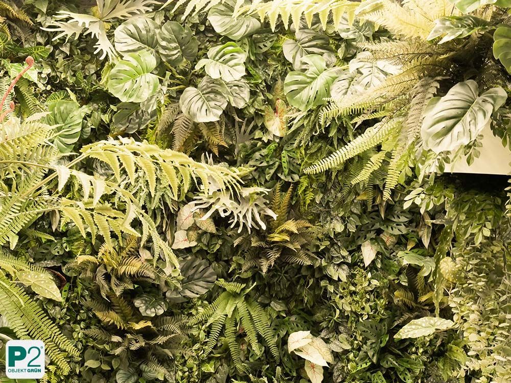 Üppig bepflanzte grüne Wand mit Farnen und tropischem Blattwerk im Innenraum.