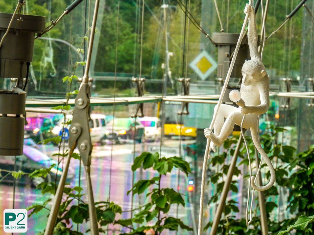 Weiße Affenfigur, die an einem Seil in einem Gewächshaus hängt.