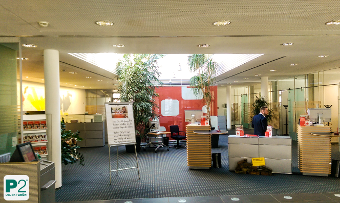 Büro mit Pflanzen, Schreibtischen und Sitzbereich, Mann arbeitet am Schreibtisch, helle Deckenbeleuchtung