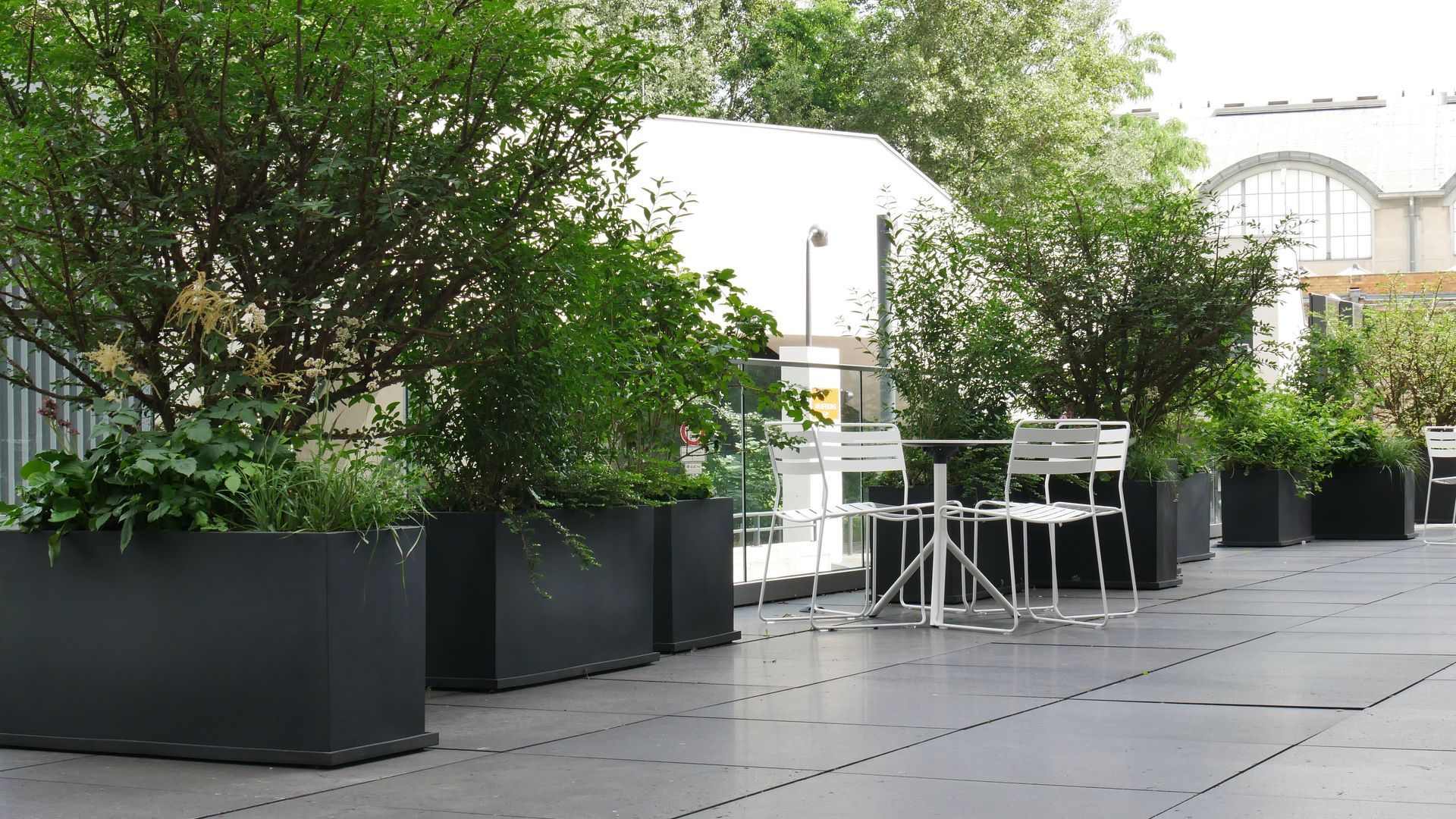 Weiße Metallstühle und -tische stehen auf einer modernen Außenterrasse