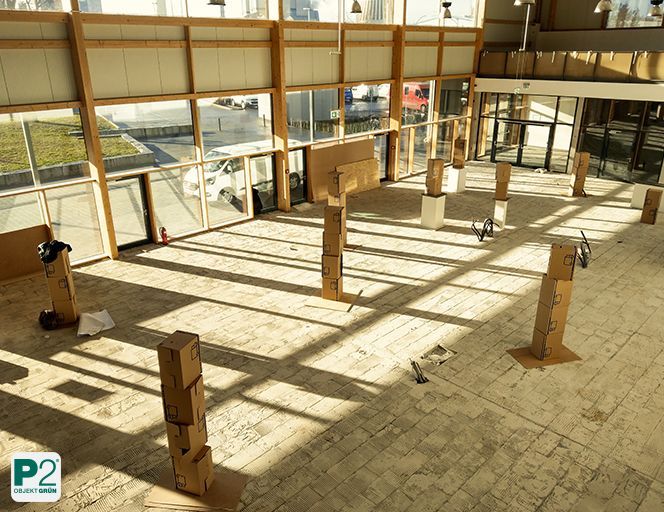 Innenraum eines Trainingsplatzes mit großen Fenstern und mehreren mit Kartons bedeckten Säulen, Sonnenlicht fällt ein