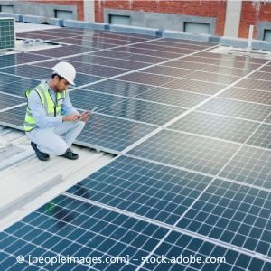 Ein Mann kniet auf einem Dach mit Solarmodulen.