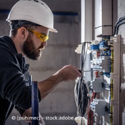 Ein Mann mit Schutzhelm und Schutzbrille arbeitet an einer Schalttafel.