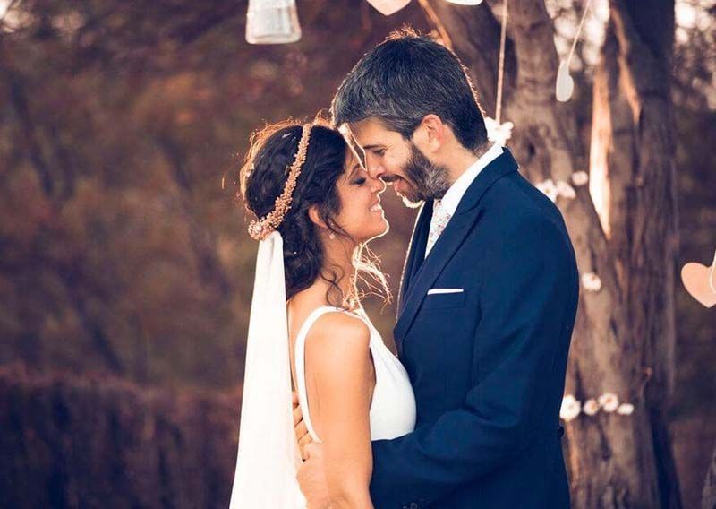 Una novia y un novio se miran delante de un árbol.