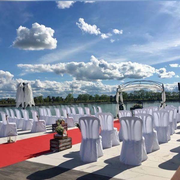 Filas de sillas blancas sobre una alfombra roja frente a un lago