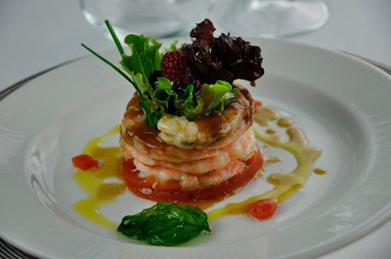 Un plato blanco cubierto con camarones, tomates y lechuga.